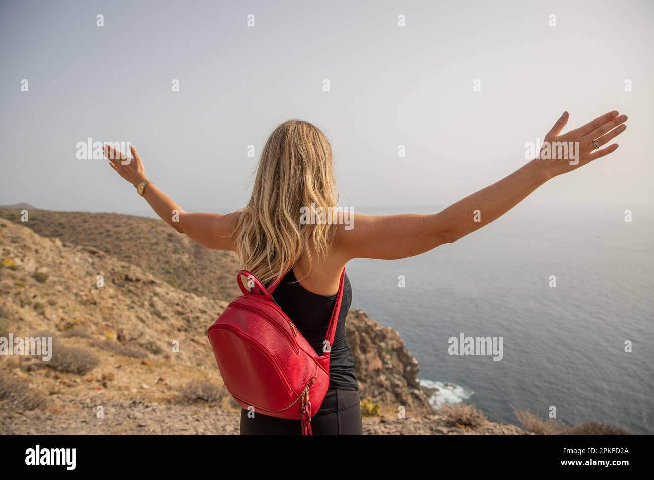 Una donna a braccia aperte osserva il mare, concetto di spensierato e di tranquillità. Foto Stock