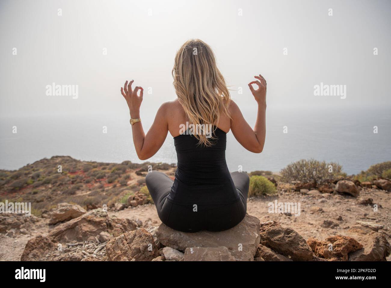 Un escursionista pratica esercizi di yoga per rilassarsi seduti su una roccia in cima alla montagna Foto Stock