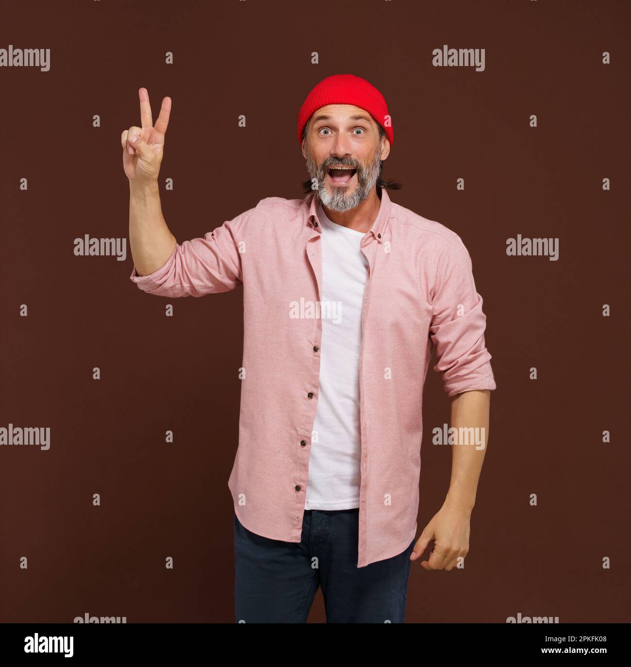 Positivo uomo caucasico europeo bello mostra gesto di V vittoria. L'uomo allegro con la barba argentata alza la mano con due dita a forma di V, indicando un gesto di vittoria, con un sorriso sul viso. Foto di alta qualità Foto Stock