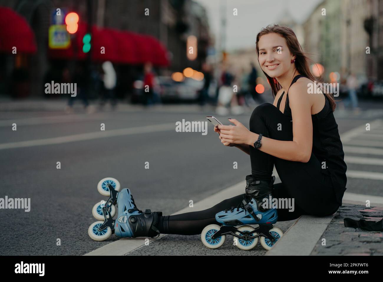 Persone attività all'aperto e concetto di ricreazione. Ripresa orizzontale di una donna sottile attiva in buona forma fisica Rides Rollerblade utilizza smartphone Foto Stock