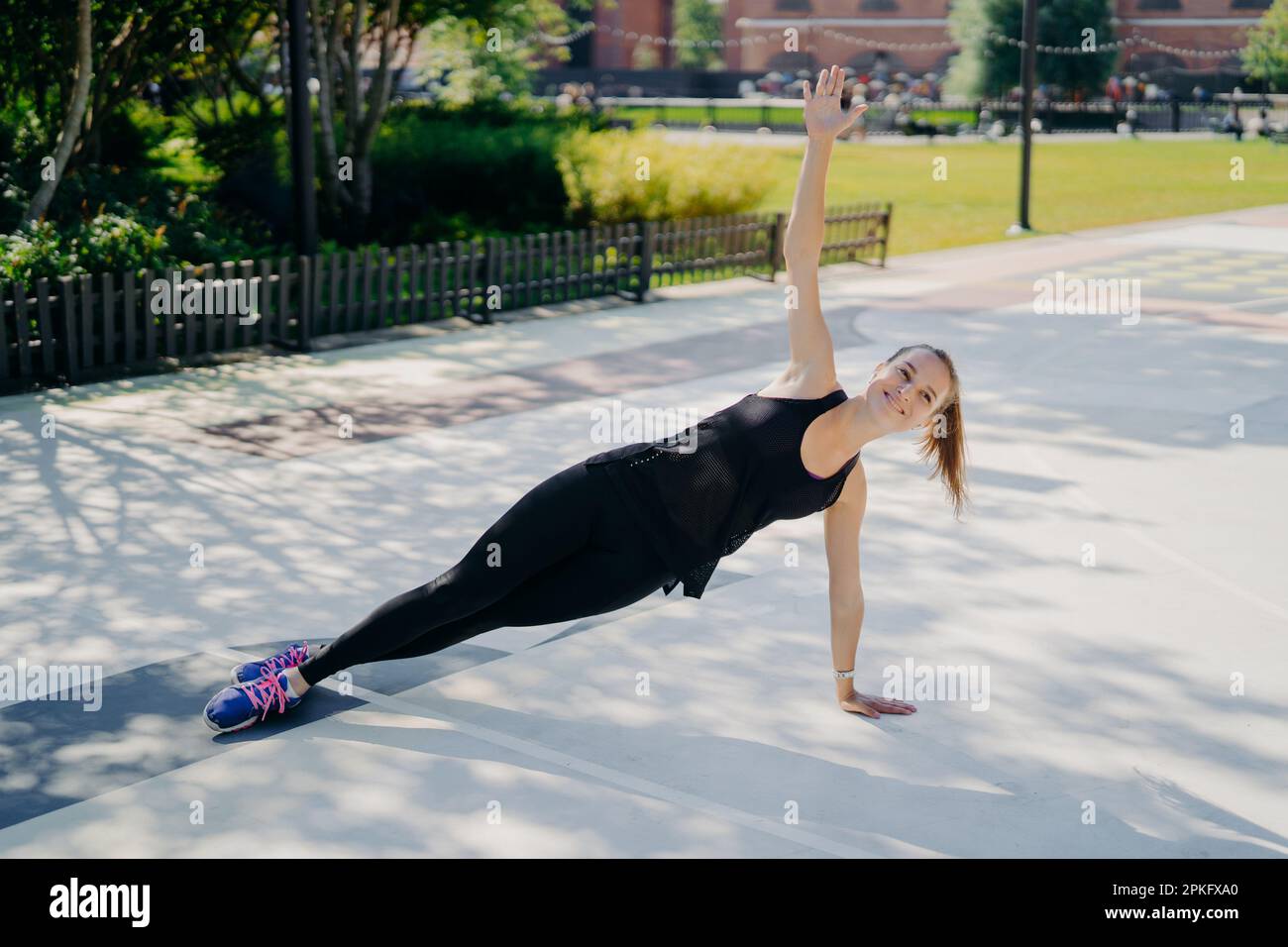 Concetto di sport e ricreazione. La donna sottile atletica si leva in fianco solleva il braccio sorrisi positivamente vestita con abbigliamento attivo porta uno stile di vita sano Foto Stock