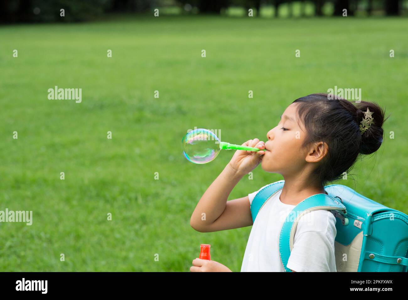 Una bambina della scuola elementare con uno zaino da scuola che gioca con bolle di sapone Foto Stock