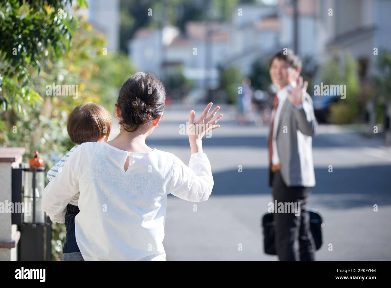 Moglie con il bambino che sventolava marito sulla sua strada per lavorare Foto Stock