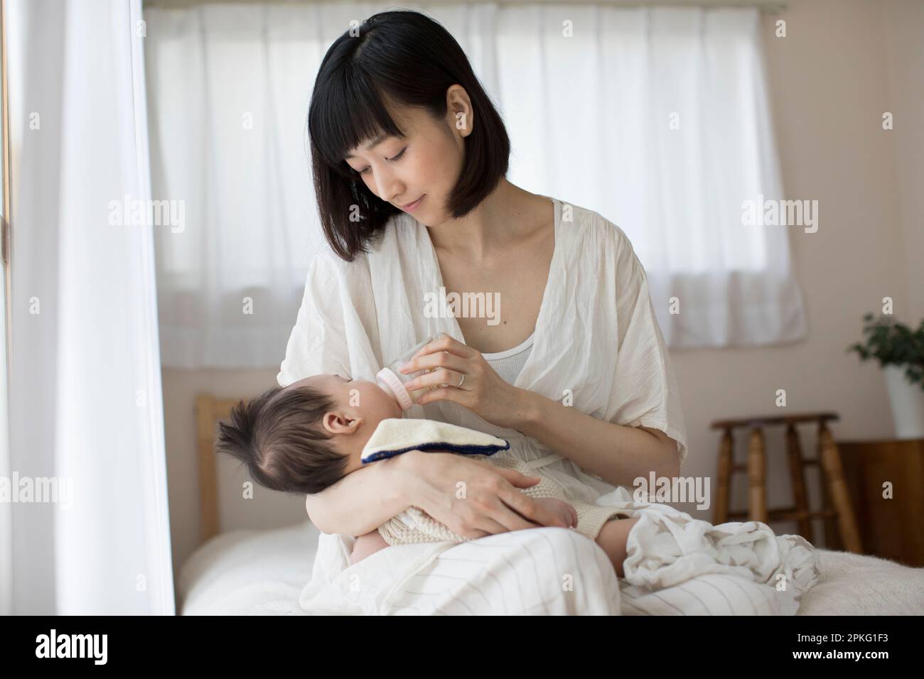 Madre che allatta il bambino con un biberon in camera da letto Foto Stock