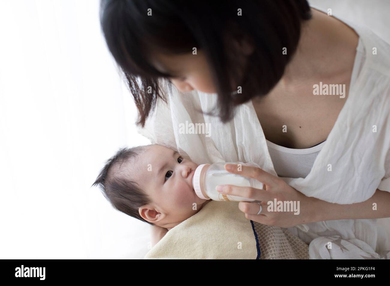 Bambino che beve latte da un biberon mentre è tenuto da madre Foto Stock