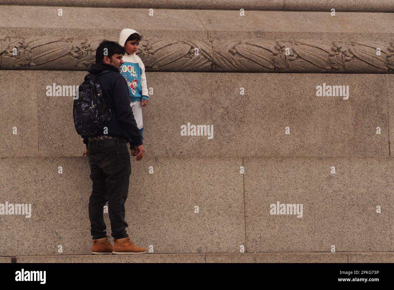 Un giovane ragazzo asiatico e suo padre in piedi sul plinto che circonda la colonna di Nelson a Trafalgar Square, Londra, Inghilterra. REGNO UNITO Foto Stock