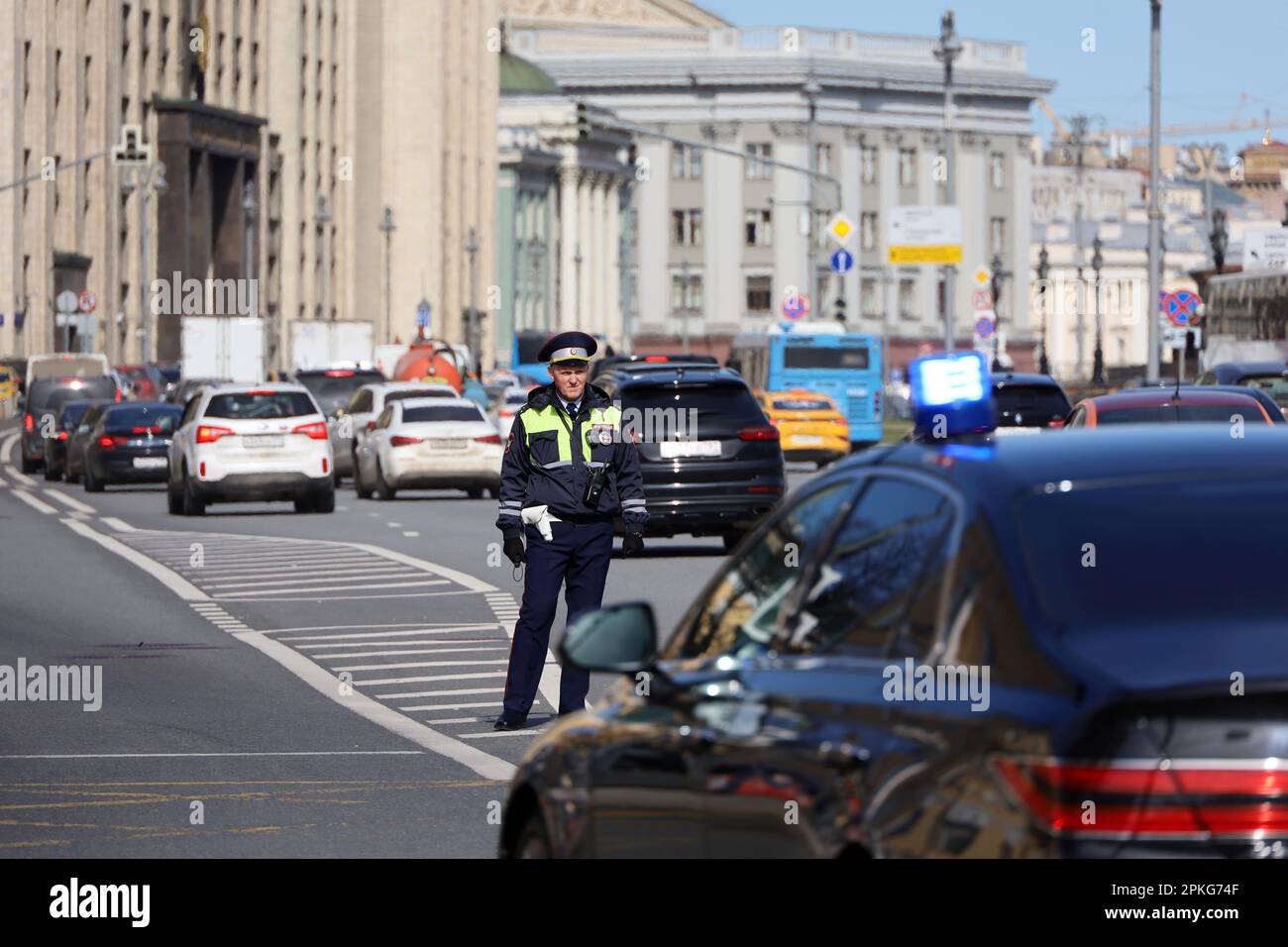 Poliziotto in piedi contro le automobili e l'edificio della Duma di Stato, auto con luce lampeggiante in primo piano. Poliziotto pattuglia la strada della città Foto Stock