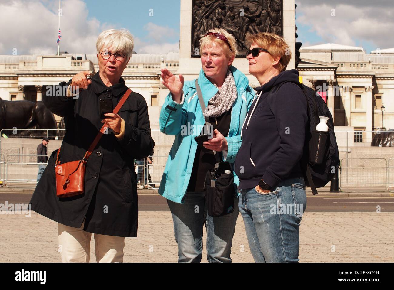 Tre donne, amici, in piedi di fronte alla colonna di Nelson, Trafalgar Square, Londra. Il Regno Unito punta a mostrare la strada da percorrere Foto Stock