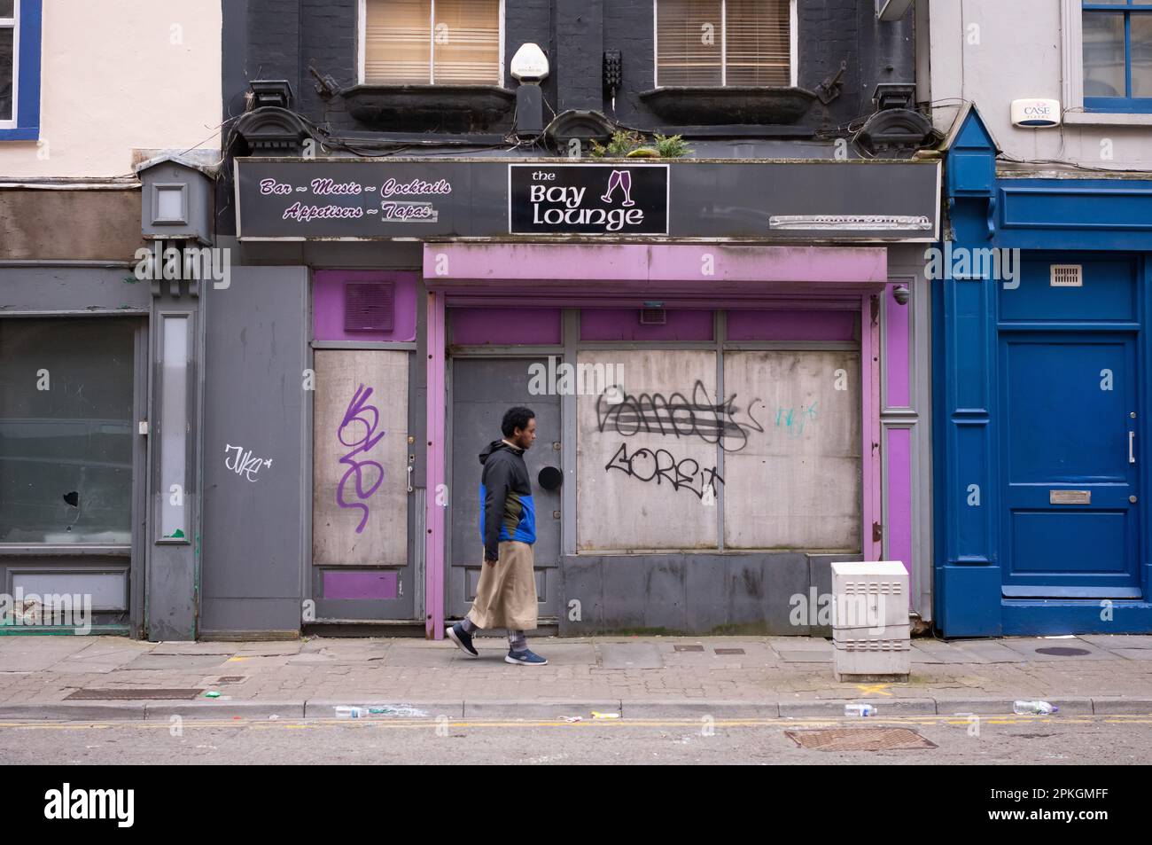 Un uomo passa davanti a un negozio chiuso a Butetown, Cardiff, Galles. Foto Stock