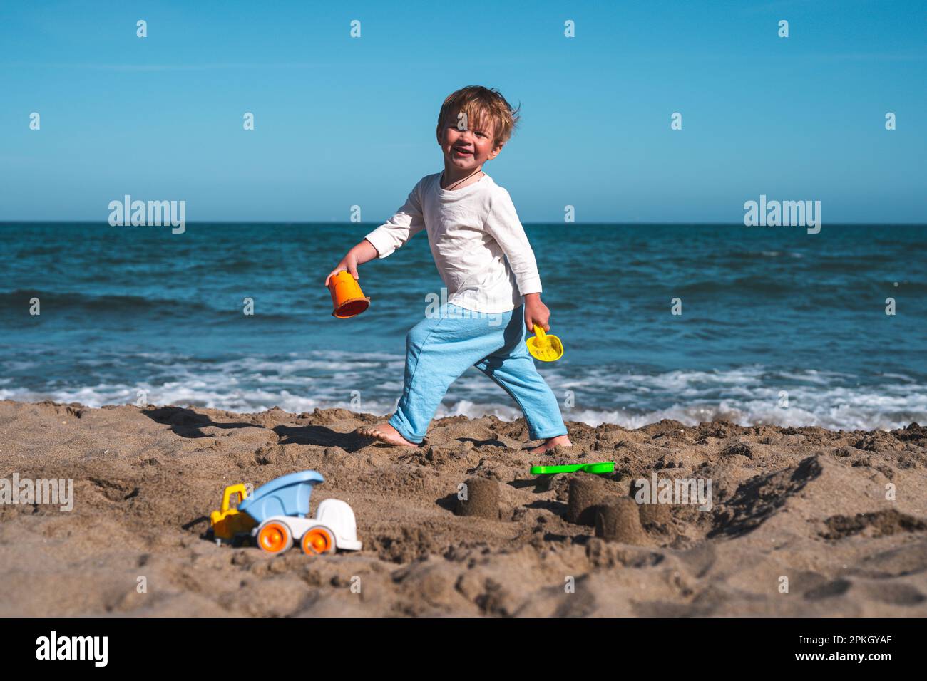 un bambino biondo di 3 anni gioca sulla spiaggia nella sabbia con i giocattoli Foto Stock