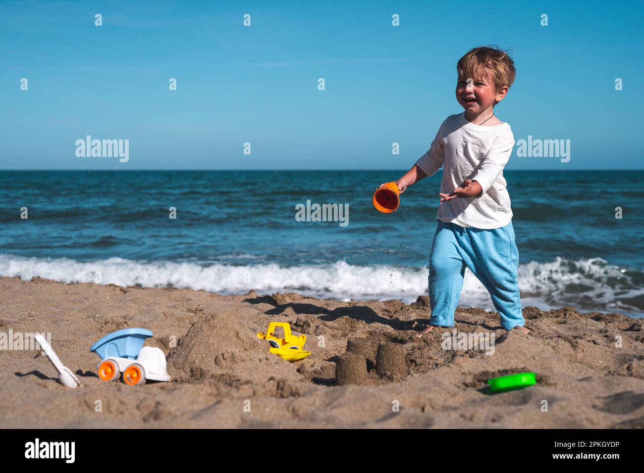 un bambino biondo di 3 anni gioca sulla spiaggia nella sabbia con i giocattoli Foto Stock