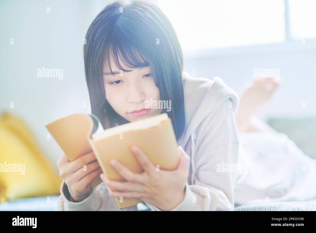 Giovane donna giaceva a letto la lettura di un libro Foto Stock