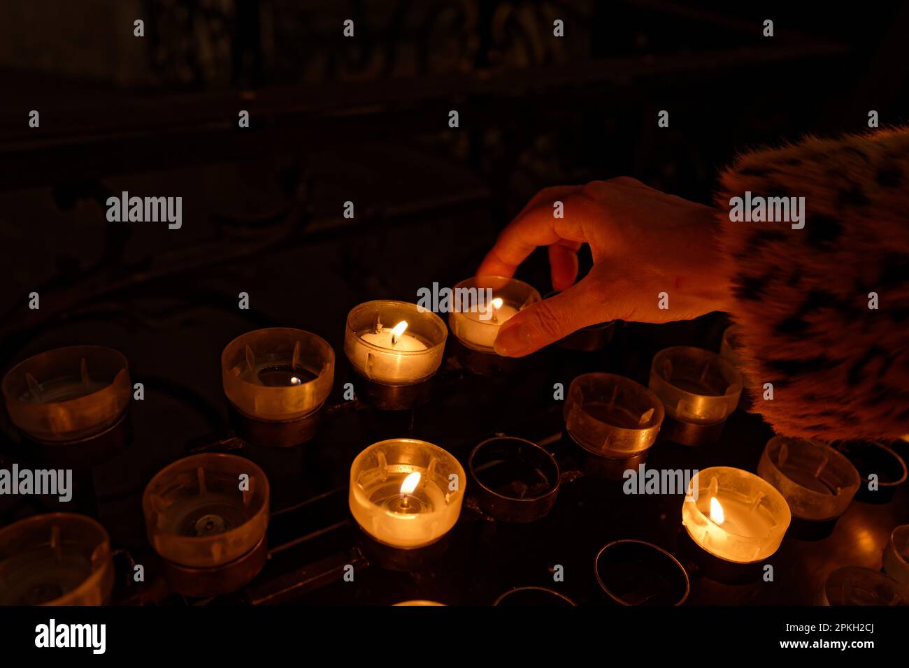 la mano di una donna mette una candela sacrificale ad un candelabro in una chiesa buia Foto Stock