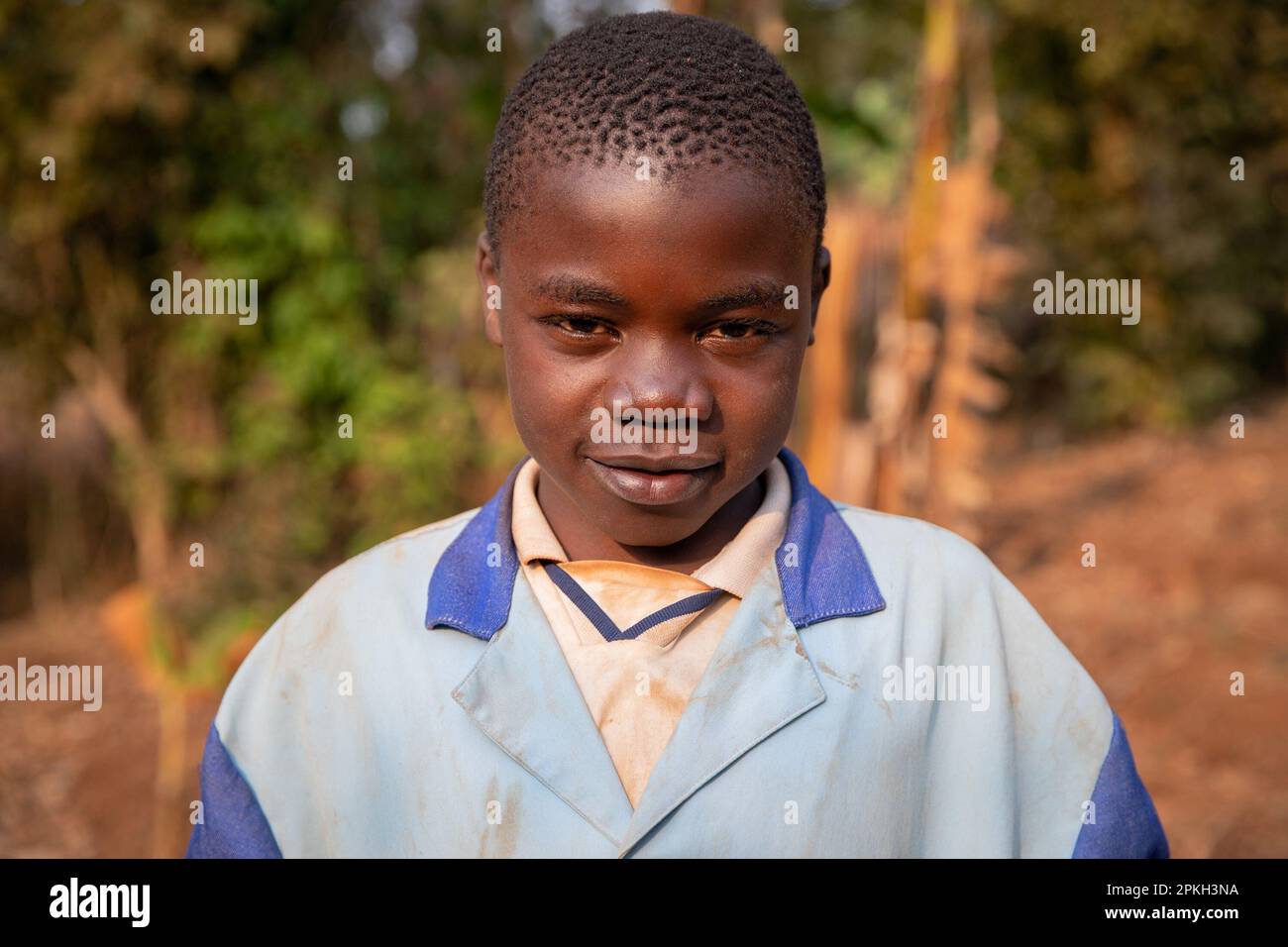 Ritratto di un bambino africano in un villaggio vestito con vestiti sporchi di terra rossa Foto Stock