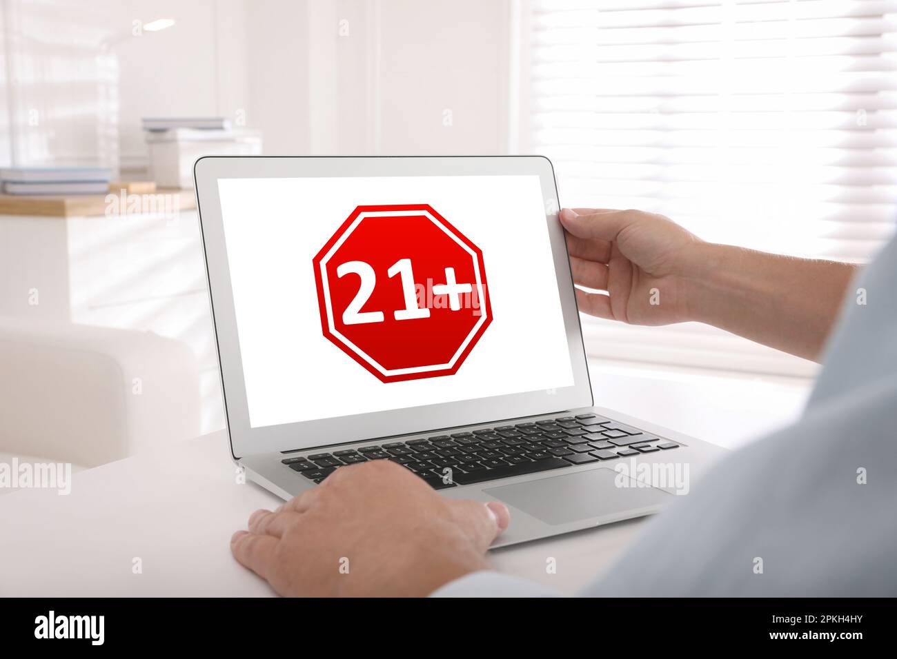 Uomo che utilizza un notebook con limite di età segno 21+ anni in ambienti chiusi, primo piano Foto Stock