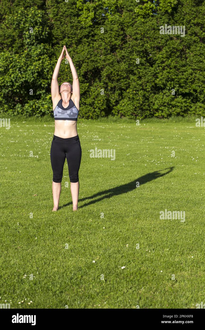 Donna (38) fare yoga in un prato nel parco, Kiel, Schleswig-Holstein, Germania Foto Stock