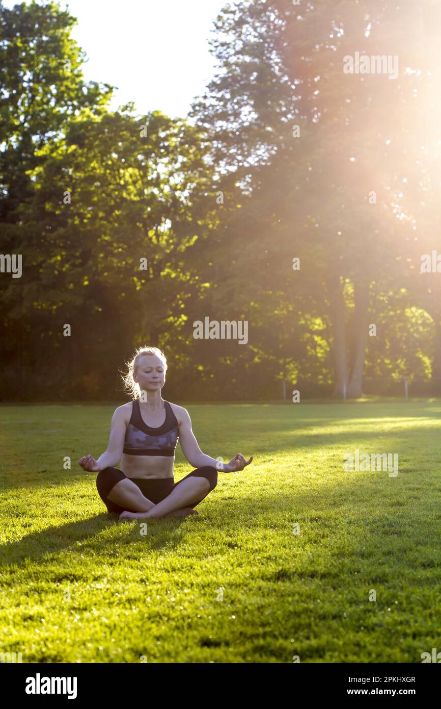 Donna (38) fare yoga in un prato nel parco, Kiel, Schleswig-Holstein, Germania Foto Stock