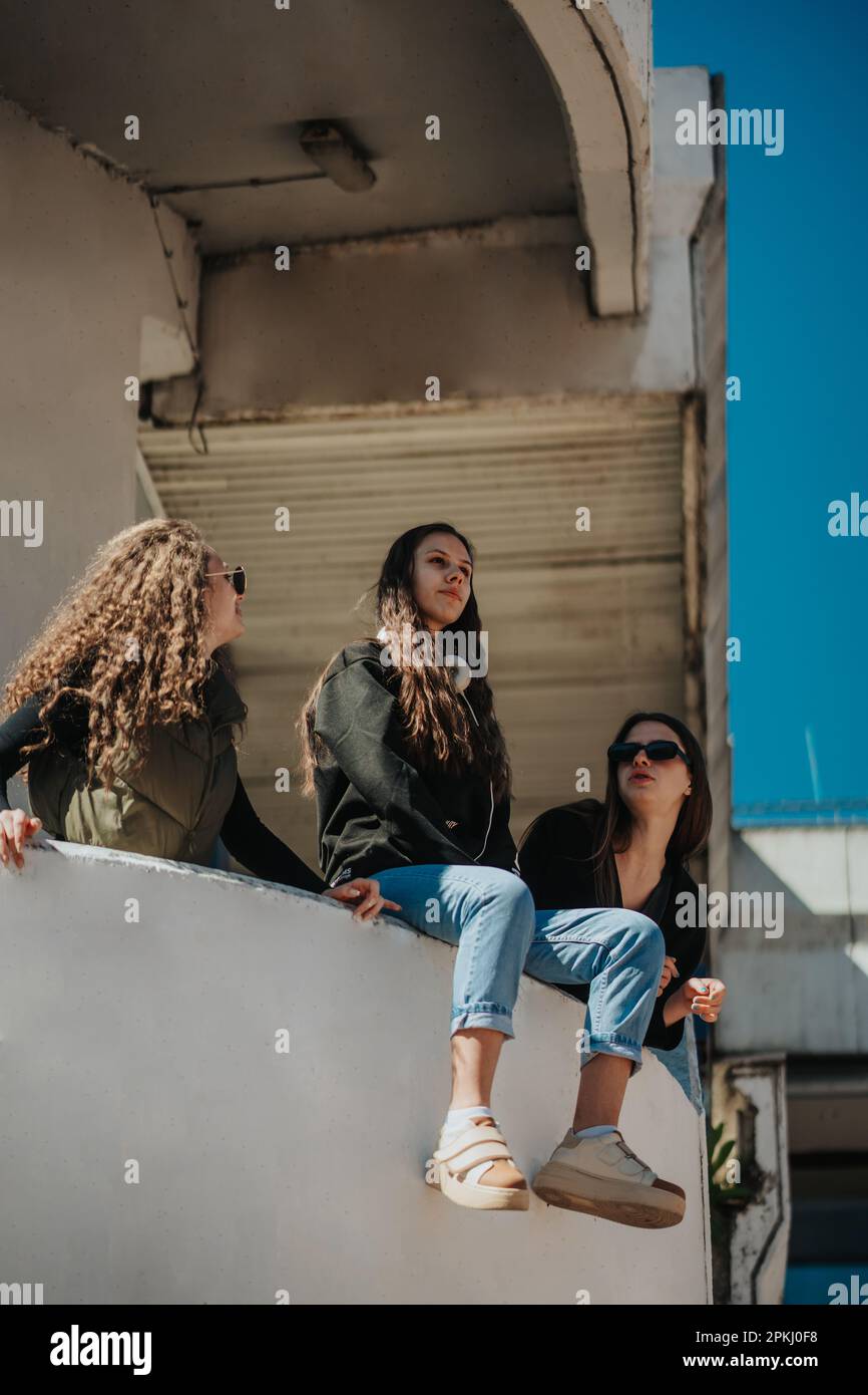 Splendida ragazza brunette seduta su un muro e pensando profondamente a qualcosa. Le sue amiche le parlano, ma non le percepisce Foto Stock