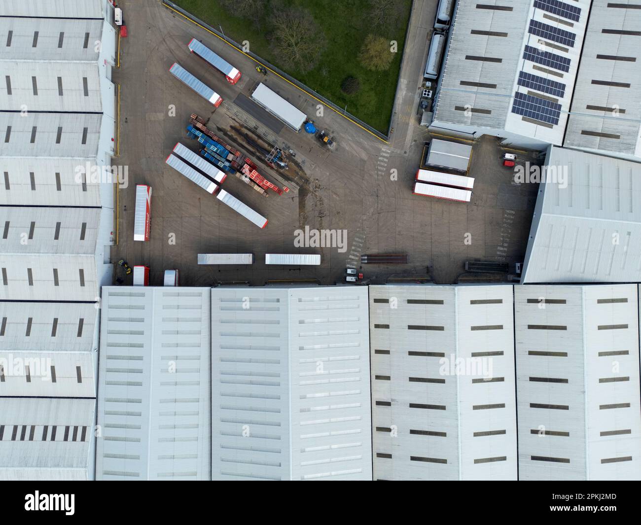 Drone vista dall'alto verso il basso di un grande magazzino che mostra pannelli solari parziali sui tetti. I camion e i rimorchi possono essere visti nel cortile. Foto Stock