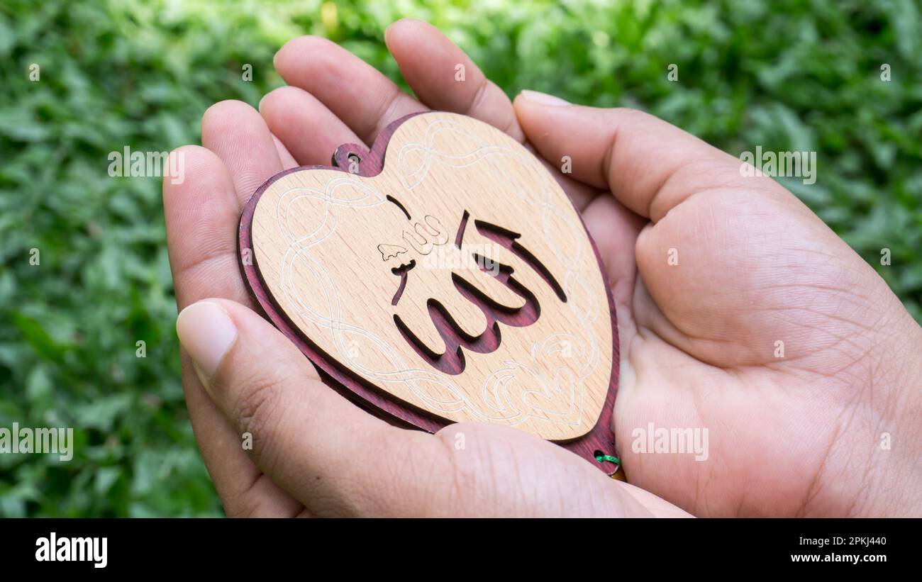 Arabo 'Allah' scritto in inglese significato di Dio. Donna musulmana che tiene le mani a forma di cuore tag Foto Stock