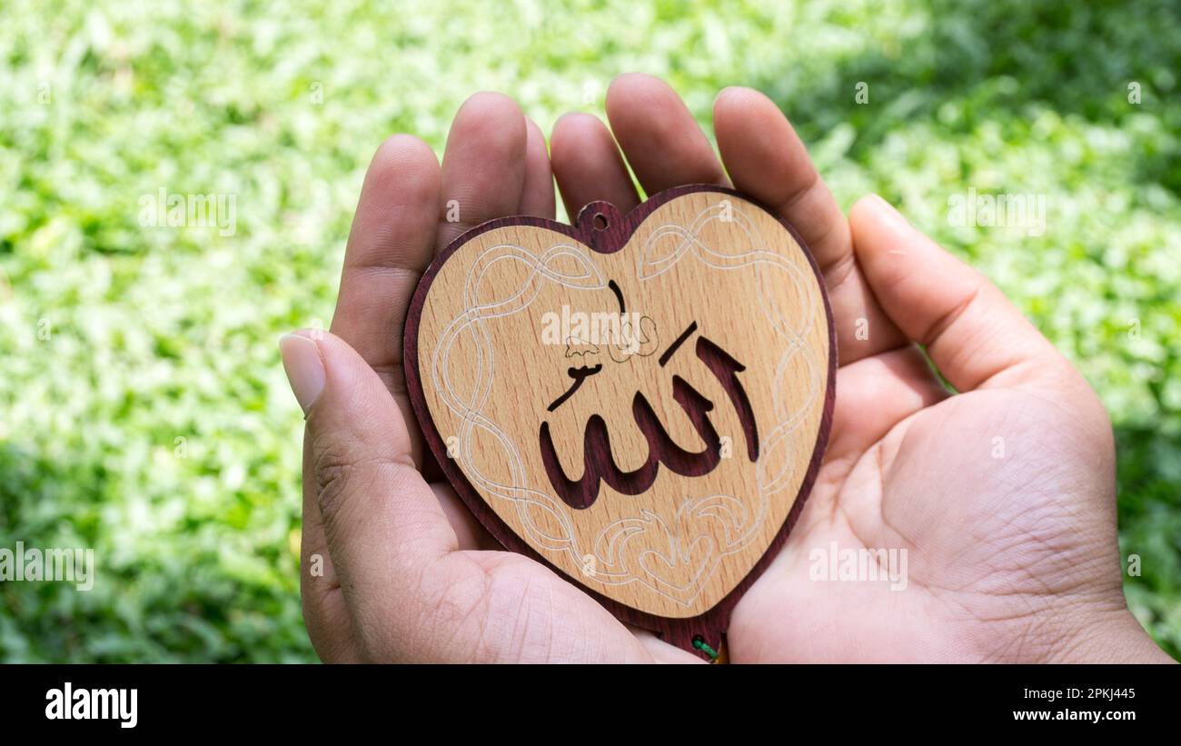 Arabo 'Allah' scritto in inglese significato di Dio. Donna musulmana che tiene le mani a forma di cuore tag Foto Stock