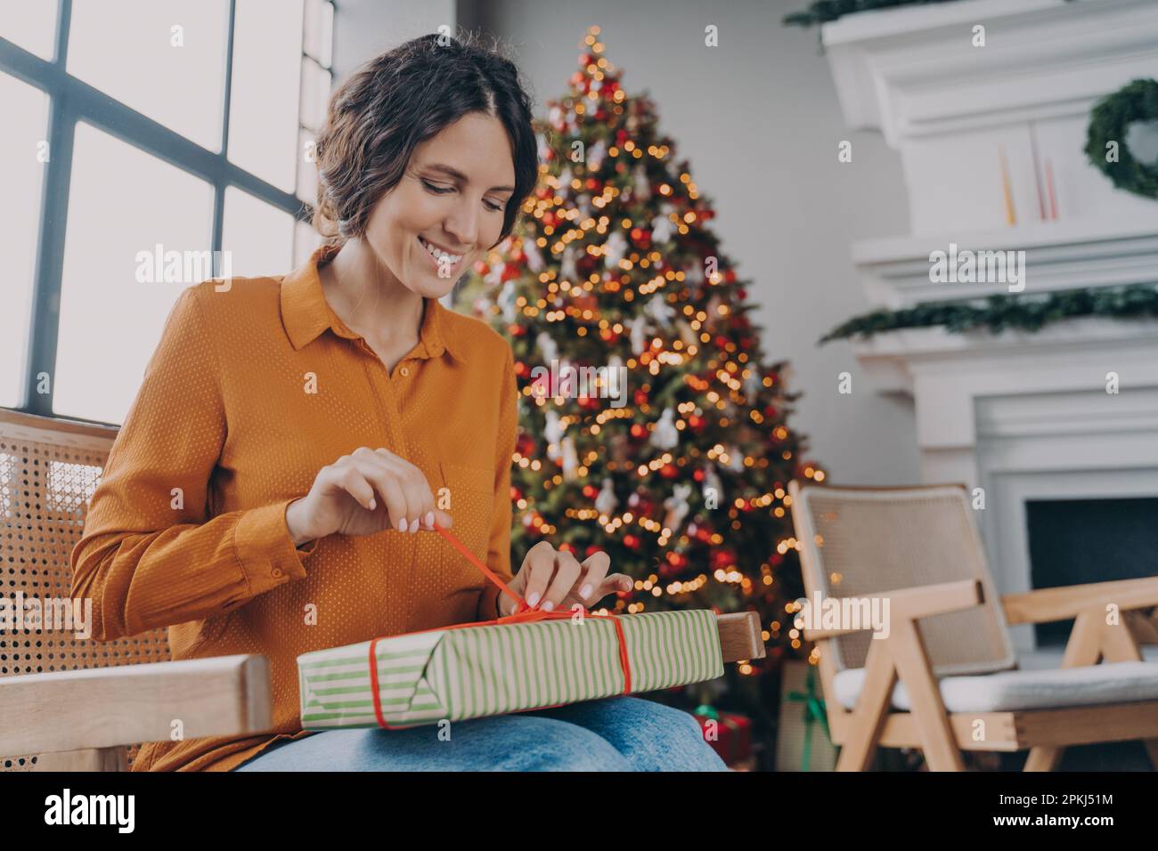 Allegra felice donna europea che disimballa regali di Natale a casa, anticipando l'umore gioioso delle prossime vacanze invernali, sorridendo donna italiana seduta in ro Foto Stock