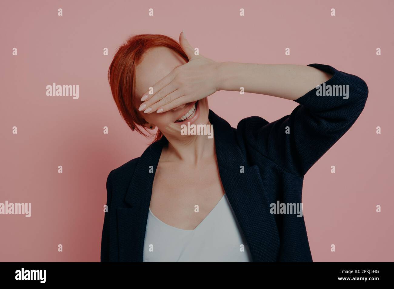 Donna zenzero positivo carino tenendo la mano davanti al viso, coprire gli occhi in previsione di qualcosa di meraviglioso, in attesa di sorpresa dal ragazzo mentre Foto Stock