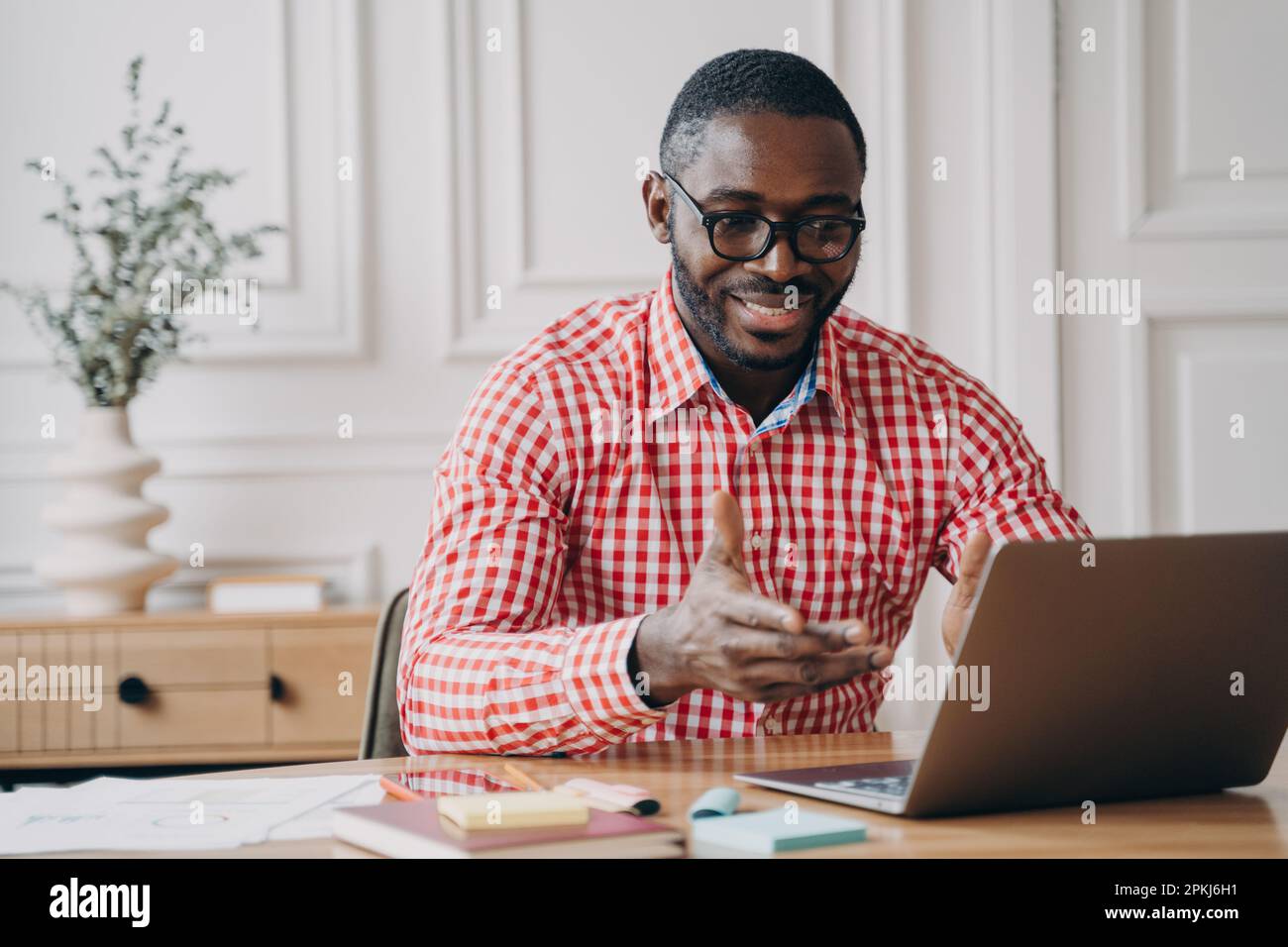 Un insegnante in linea uomo africano positivo che guarda lo schermo del laptop e sorridente, che parla con gli studenti mentre lavorano a distanza da casa, vestito di cas Foto Stock