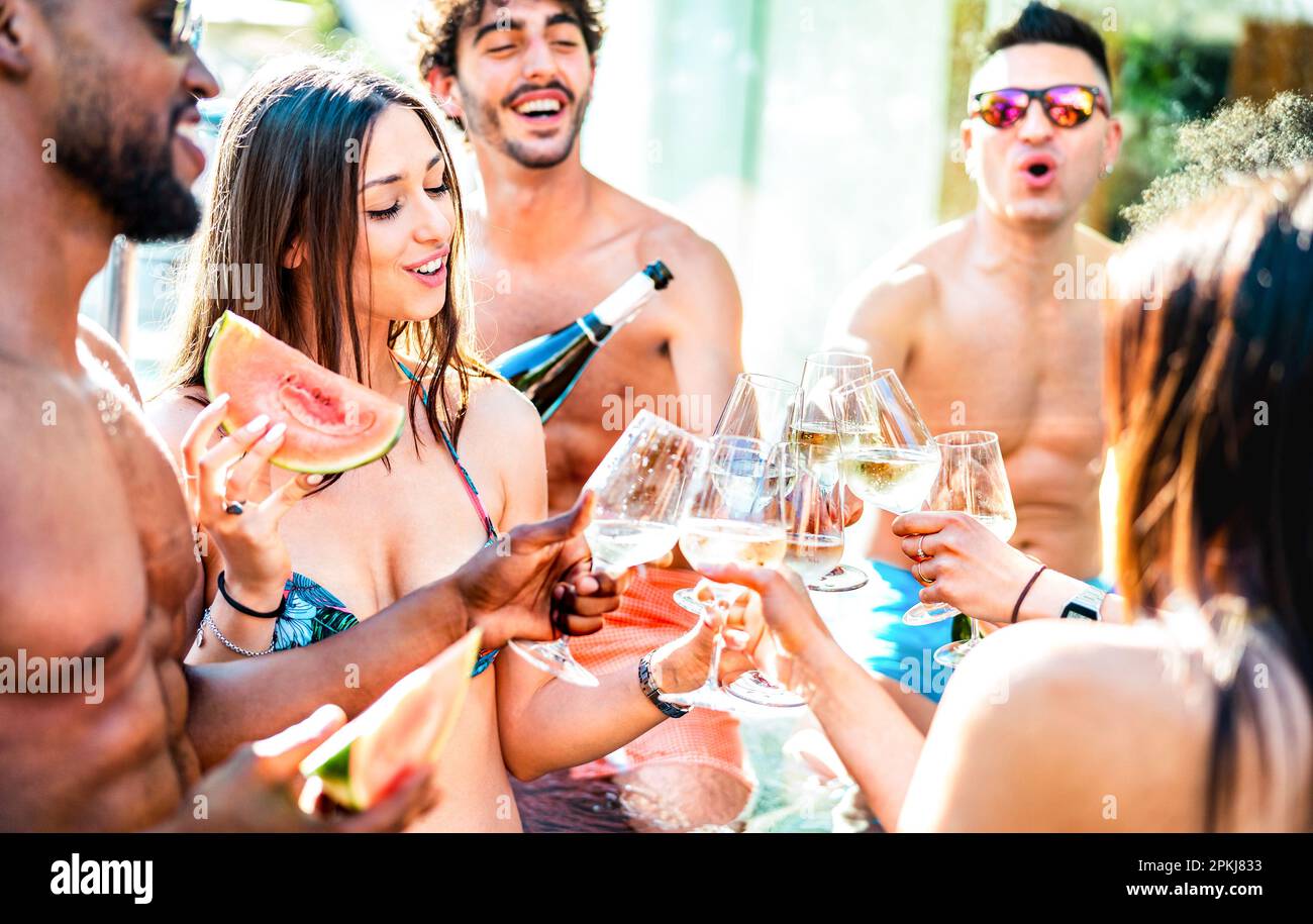 Gruppo di amici alla moda che beve champagne bianco alla festa a lato della piscina privata - concetto di vacanza stile di vita con giovani uomini e donne che si divertono Foto Stock