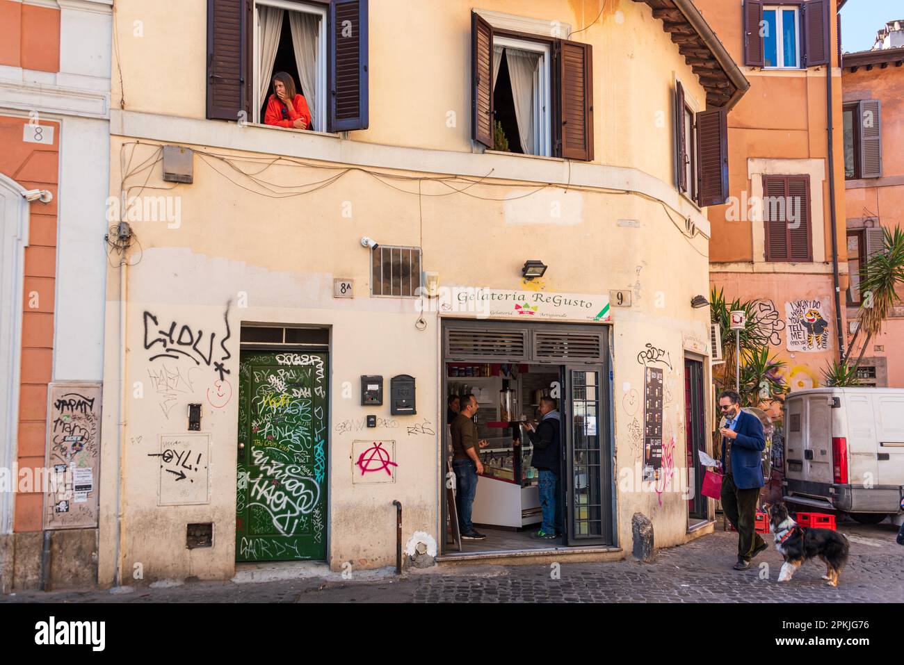 Straßencafe, Italien, mai 2023 am Frühen Morgen in Trastevere. Eine Frau schaut aus dem Fenster, ein Mann mit Hund geht vorbei Foto Stock