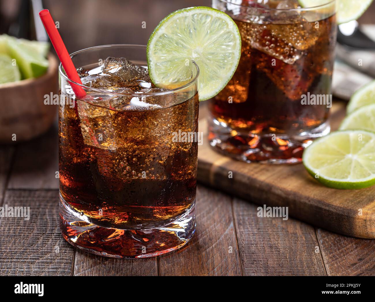 Cocktail al rum e alla cola con fettina di lime su un tavolo rustico in legno. Primo piano Foto Stock