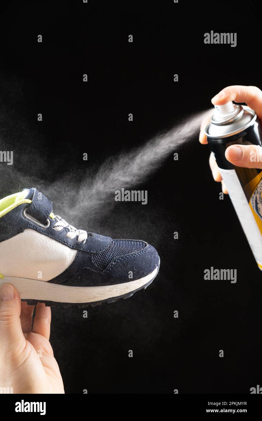 Una donna applica uno spray da un cilindro con un liquido idrorepellente alla scarpa per bambini. Cura delle scarpe, eliminazione degli odori sgradevoli. Foto Stock