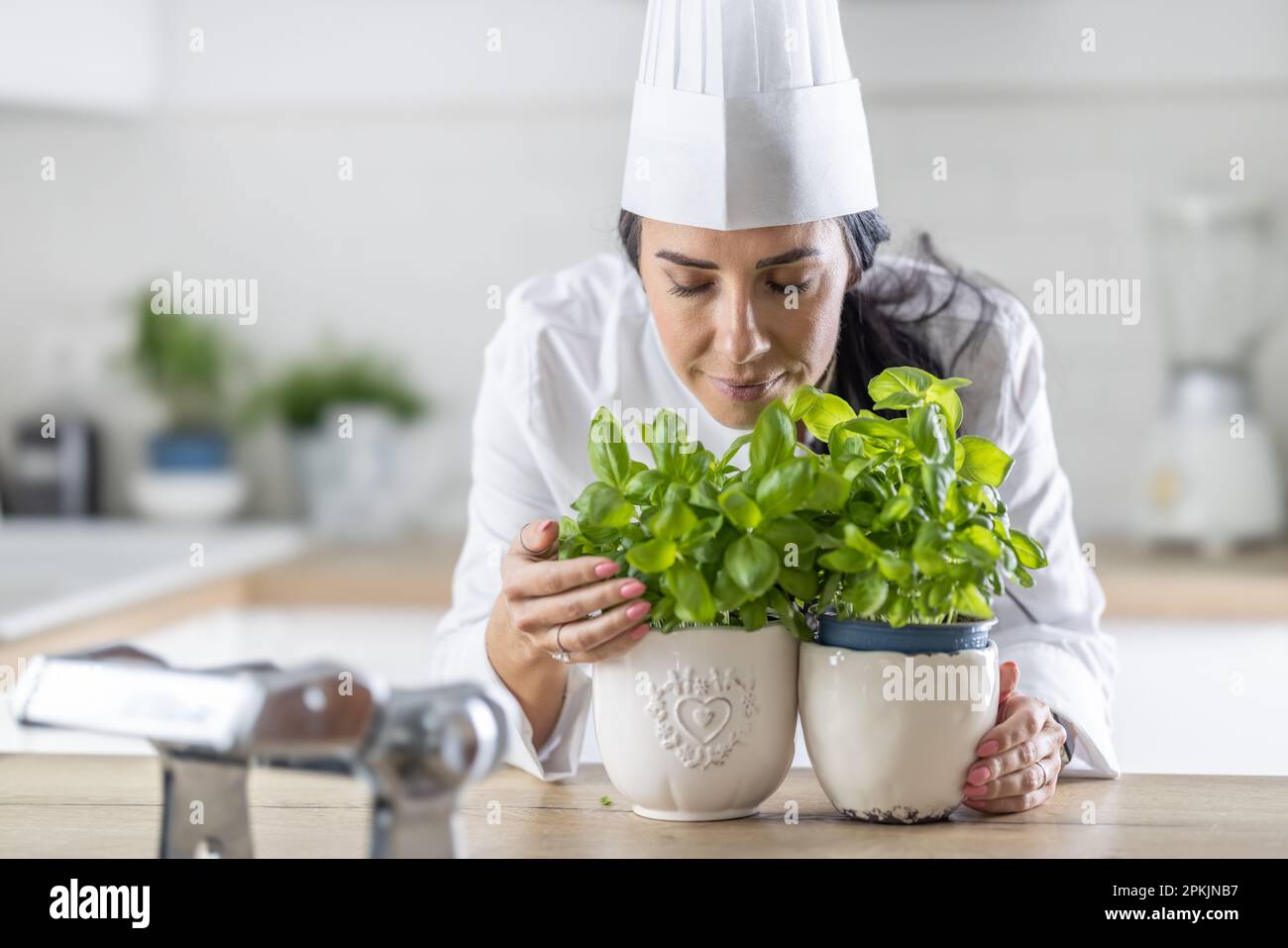 Cuoco femminile professionista in cappello bianco chiude gli occhi come lei odora basilico fresco in pentole di fronte a lei. Foto Stock