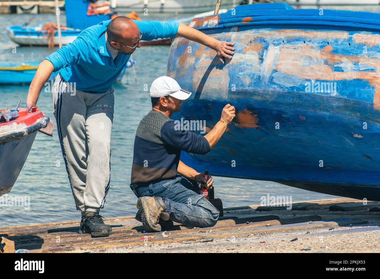 Pescatore che ripara e dipinge un vecchio peschereccio in legno al molo portuale di Bari, Puglia Foto Stock