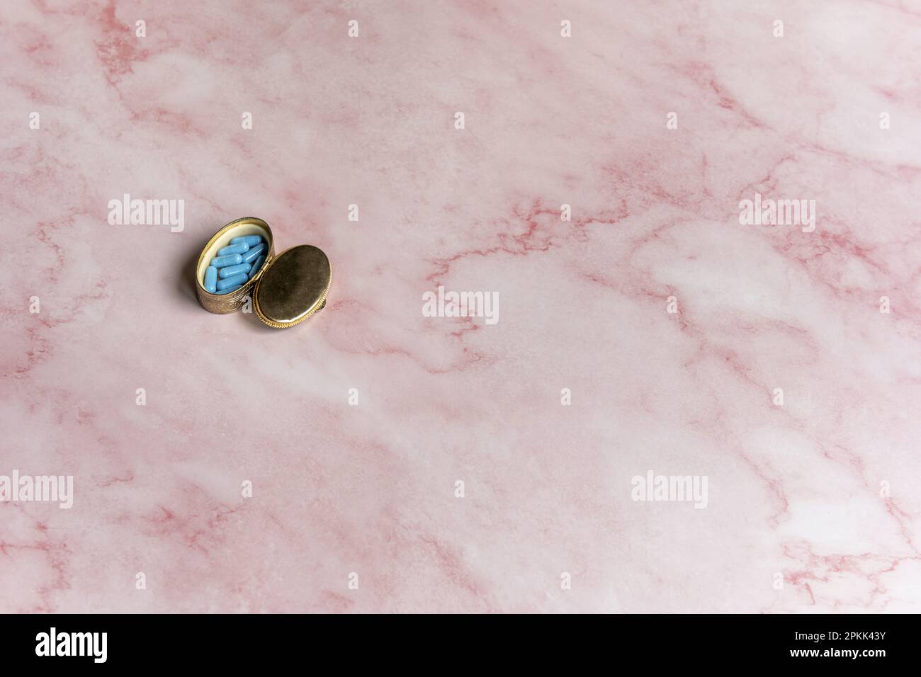 Una piccola scatola di metallo usata come scatola delle pillole su una superficie di marmo rosa Foto Stock