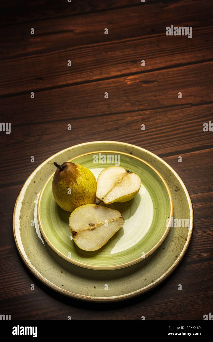 Alcune pere fresche su alcuni piatti circolari verdi su un tavolo di legno scuro Foto Stock