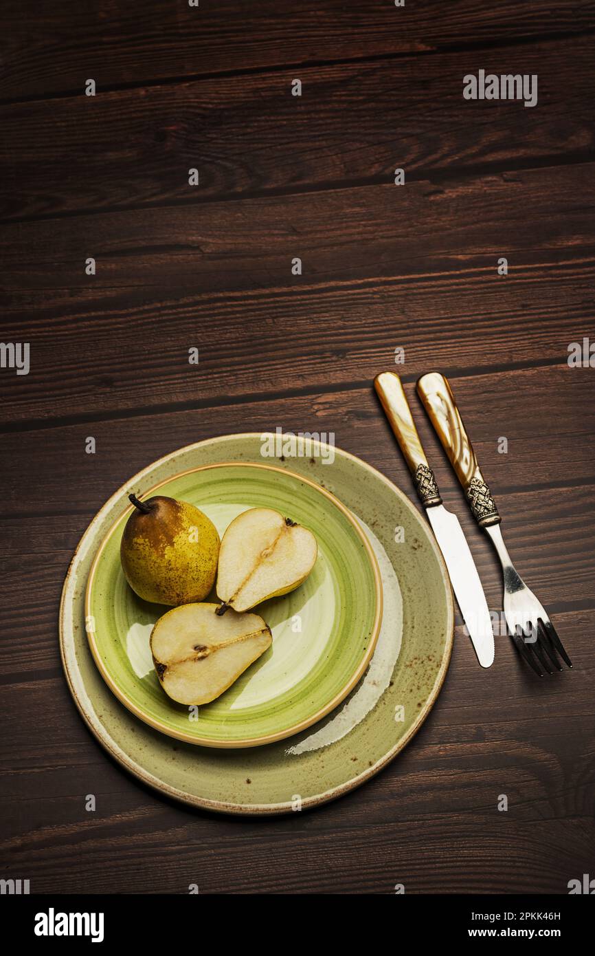Alcune pere fresche su piatti circolari verdi con posate in stile vintage su un tavolo di legno scuro Foto Stock