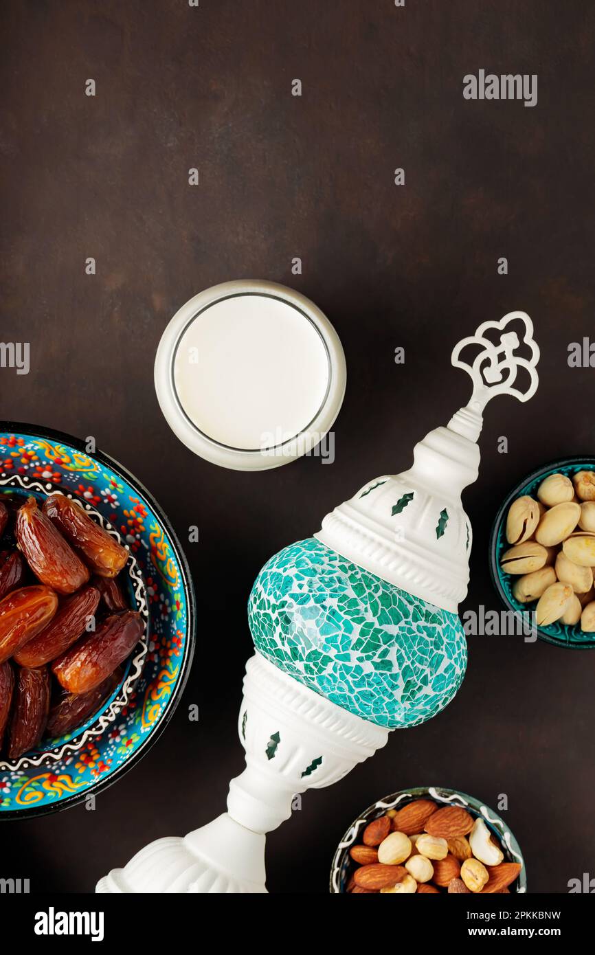 Datteri secchi, noci e latte su sfondo scuro. Ramadan Kareem e iftar cibo musulmano e lampada turca. Concetto Ramadan. Vista dall'alto Foto Stock