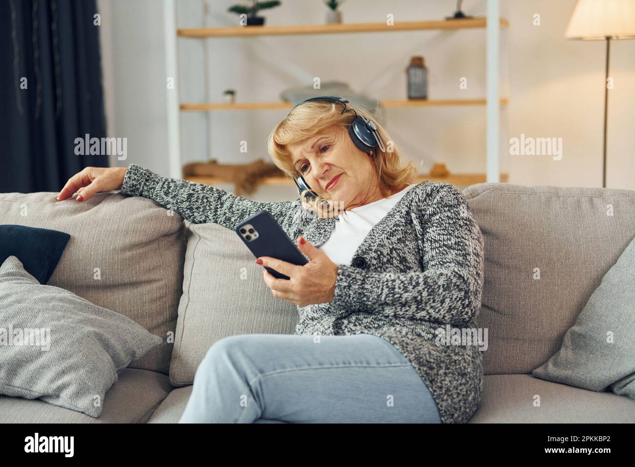 Ascolto di musica con le cuffie. Donna anziana con capelli biondi è a casa. Foto Stock