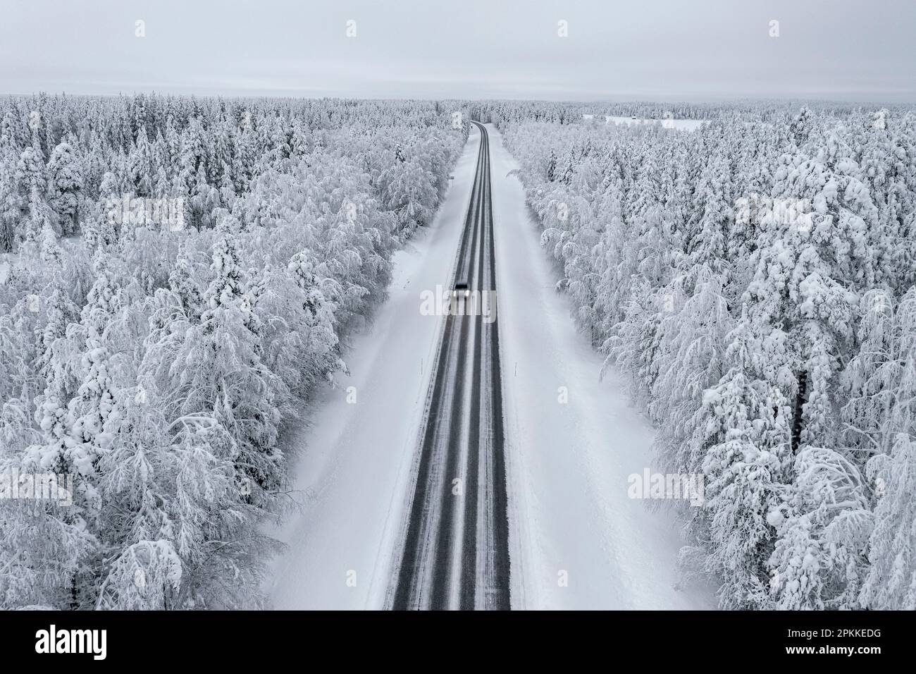 Vista dall'alto della vettura che guida su una strada vuota scivolosa nella foresta innevata, in Lapponia, Finlandia, Europa Foto Stock