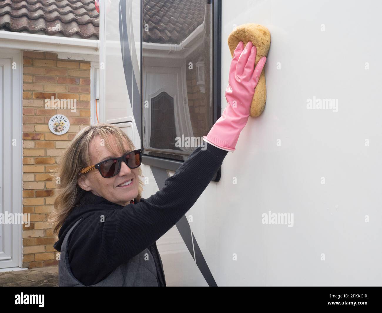 Sorridendo e guardando la macchina fotografica una mano attraente del proprietario del motorhome della signora lava il suo veicolo ricreativo con una spugn.She indossa i guanti dentellare e la lente d'ingrandimento Foto Stock
