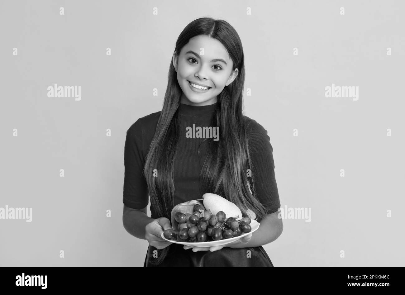 il bambino sorridente tiene il piatto di frutta fresca su sfondo giallo. Foto Stock