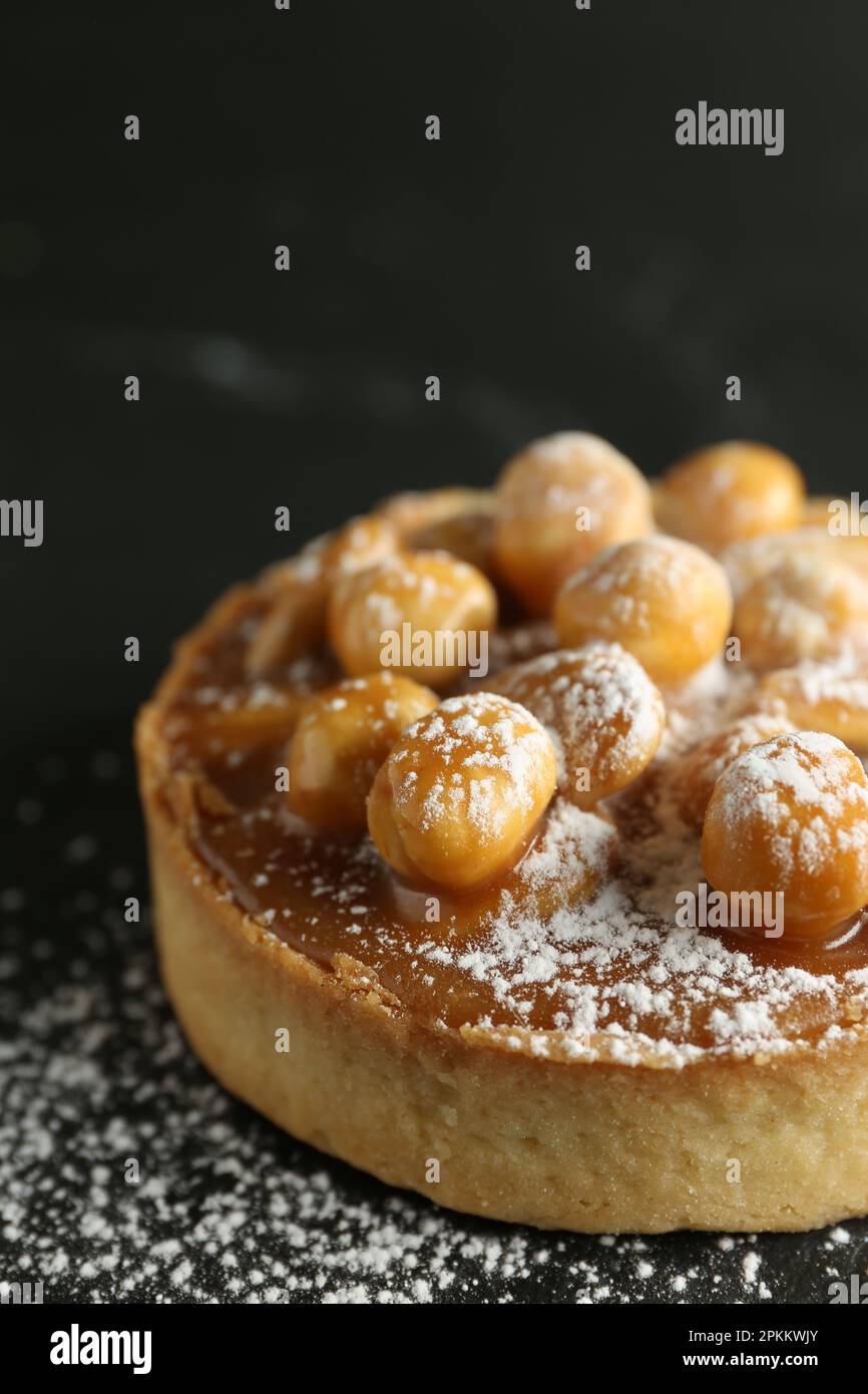Crostata deliziosa con nocciole, caramello dolce e zucchero a velo su tavola nera, primo piano Foto Stock