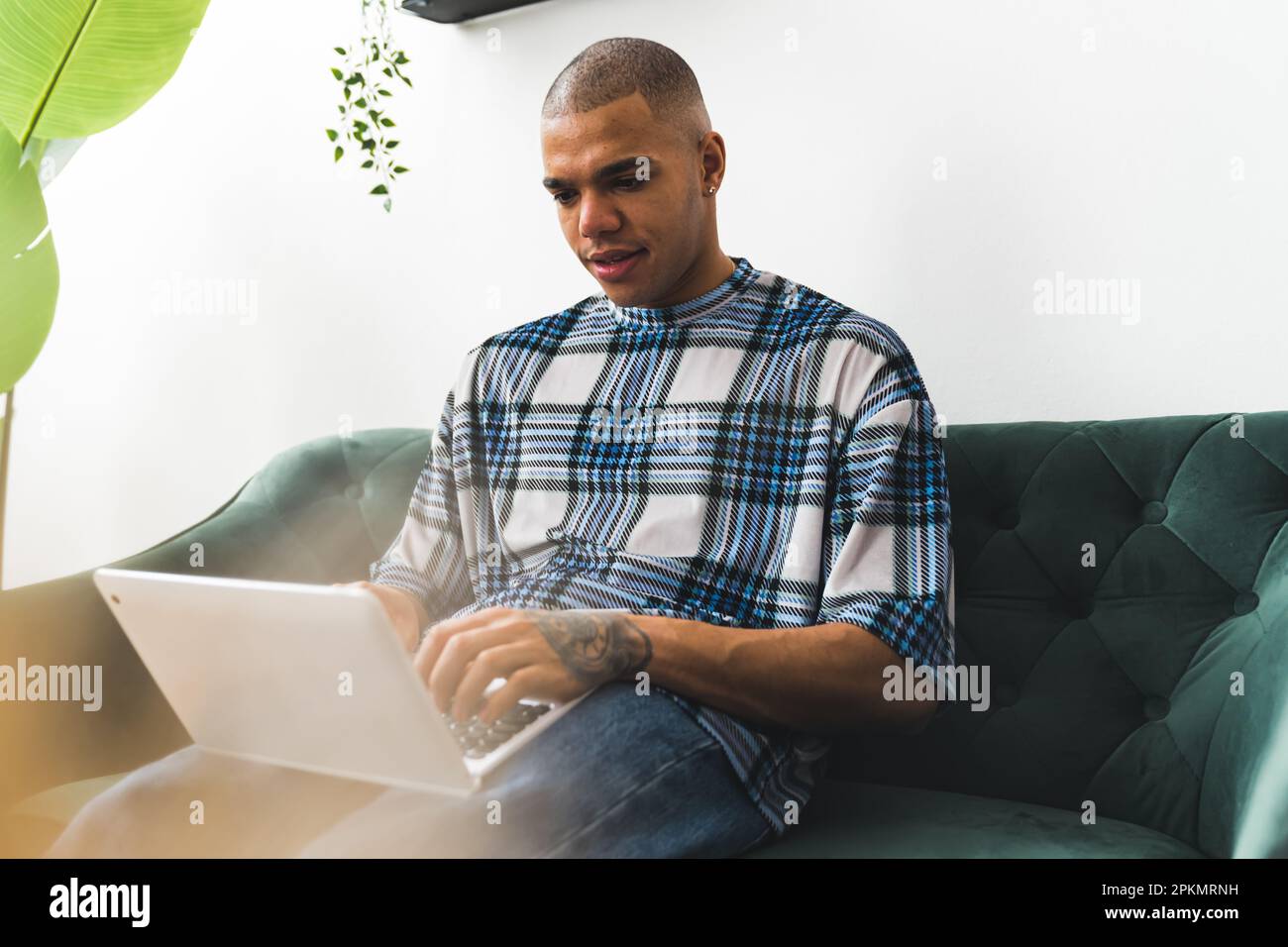 Scatto di un bel giovane uomo che usa il suo computer portatile mentre si siede su un divano a casa, mediamente pieno scatto. Foto di alta qualità Foto Stock