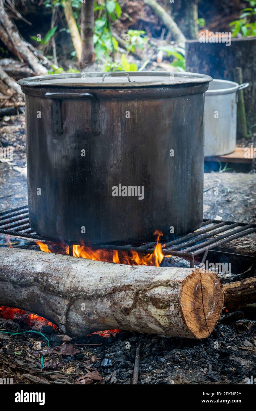 Un fuoco brucia e distilla un bollitore nero di ayahuasca in Perù Foto Stock
