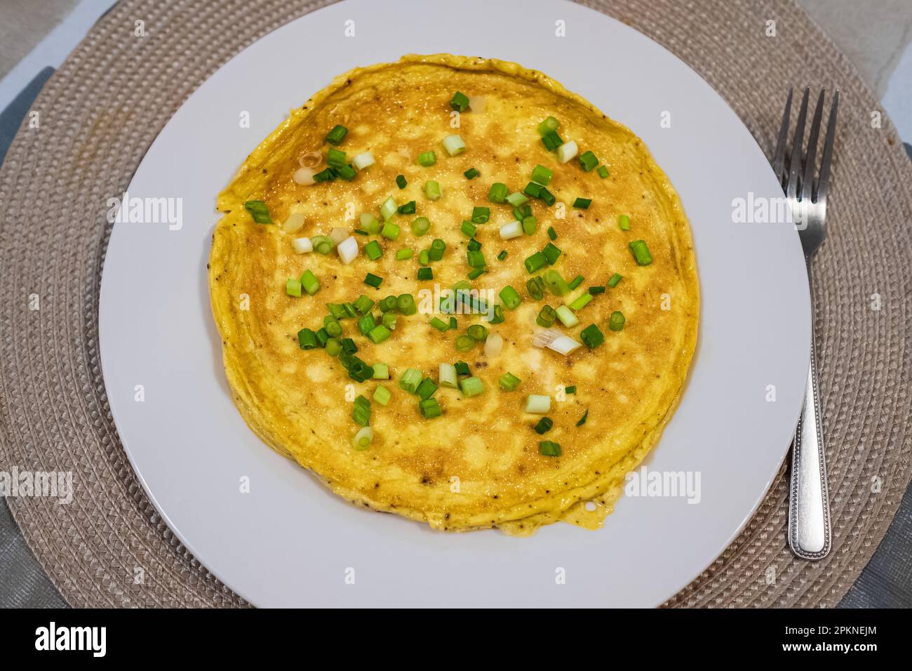 Semplice omelette all'uovo con erbe su piatto bianco. Soffice omelette da colazione con cipollotti verdi. Colazione con uova fritte in padella. Dieta chetogenica keto. Foto Stock