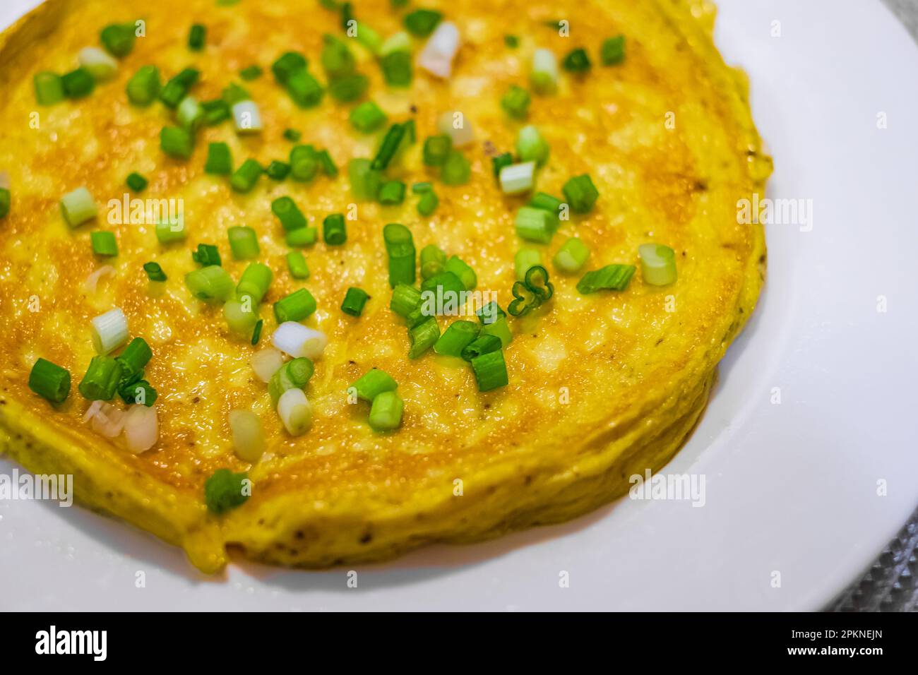 Semplice omelette all'uovo con erbe su piatto bianco. Soffice omelette da colazione con cipollotti verdi. Colazione con uova fritte in padella. Dieta chetogenica keto. Foto Stock