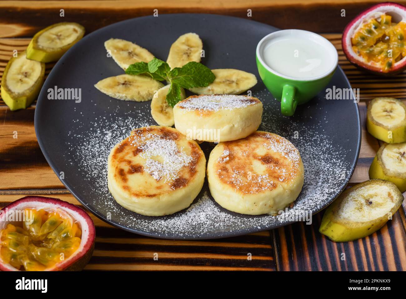 Syrniki o frittelle al formaggio con salsa di panna e banane su un piatto sul tavolo di legno primo piano Foto Stock