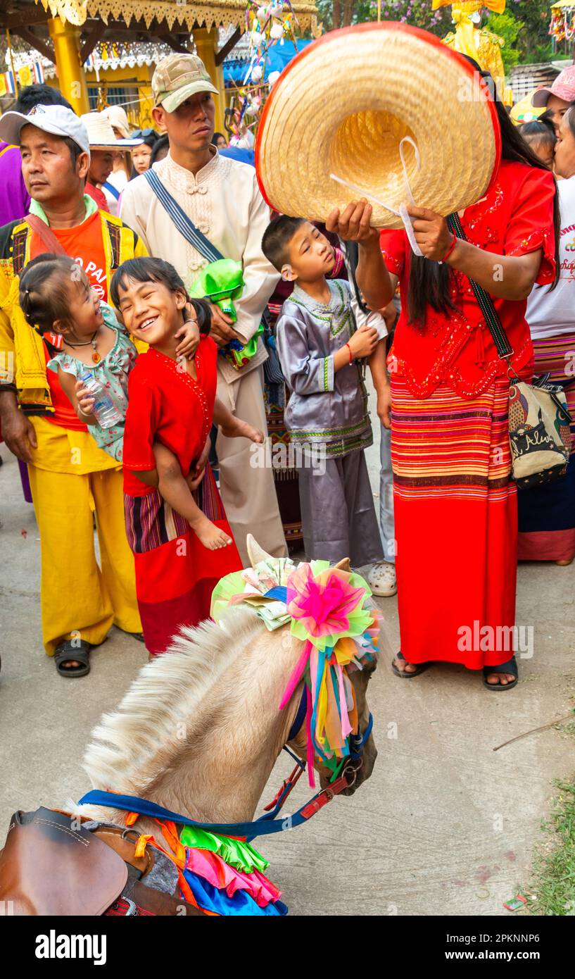 PAI, Thailandia del Nord-Aprile 4th 2023: Una folla guarda sopra, come un cavallo vestito di garb cerimoniale crolla, ed è aiutato da una donna, che usa il suo grande ha Foto Stock