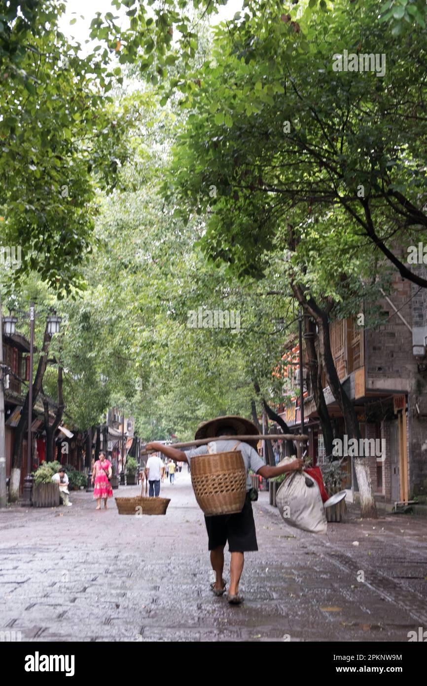 Un uomo cinese porta sulle spalle sacchi pesanti attaccati ad un bastone di bambù a Fenghuang, Cina. Foto Stock